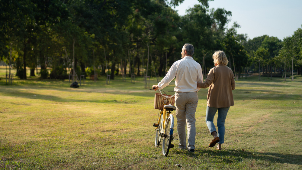 Elderly couple enjoying walking through a park with a bike