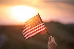 A hand holding up a small American Flag in a sunset.