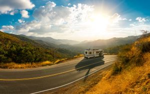 An RV driving down a road through the mountains.
