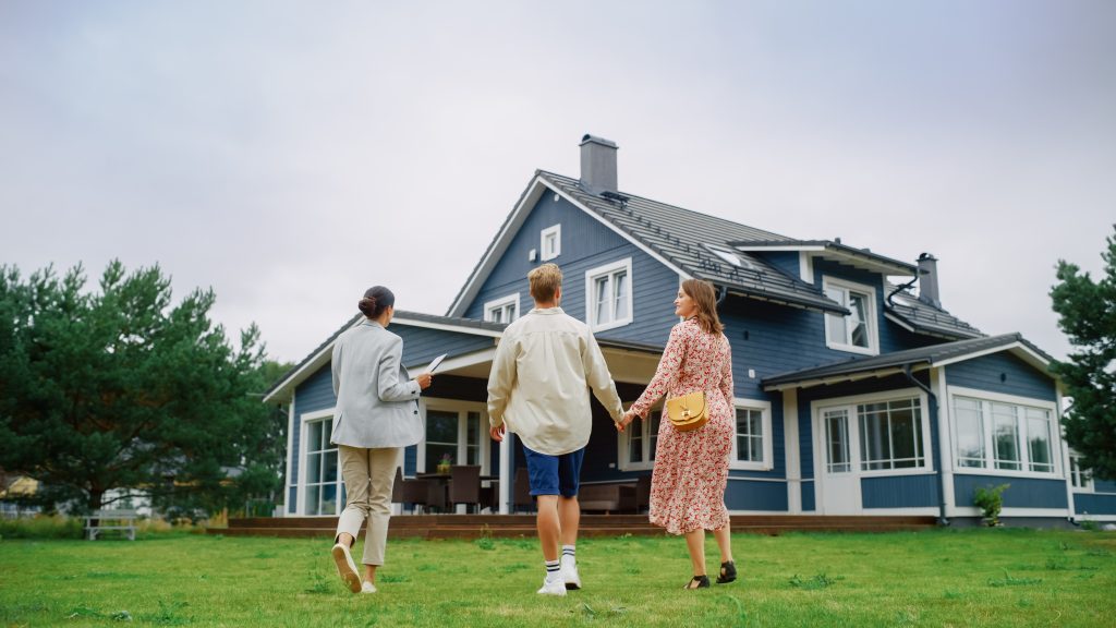 A realtor showing a house to a couple on the front lawn.