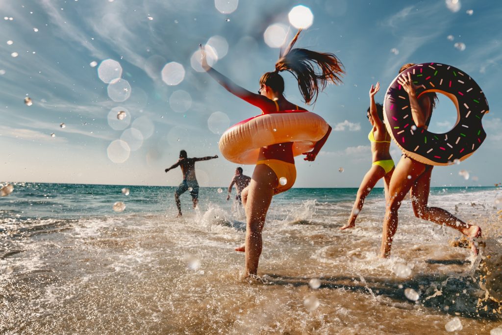 People in swimsuits splashing into the ocean with innertubes.