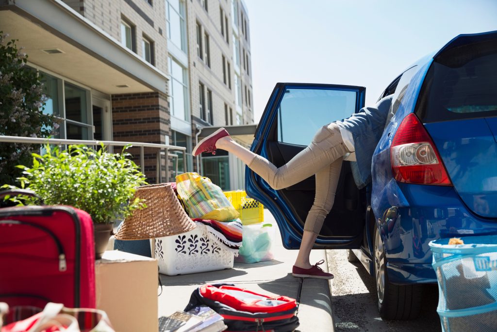 A college student unpacking a lot of stuff from a car onto a curb.