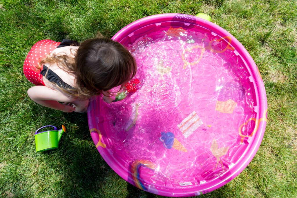 A young girl playing in a pink kiddie pool.