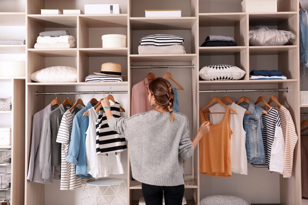A woman standing in a walk-in closet, looking at her clothing.