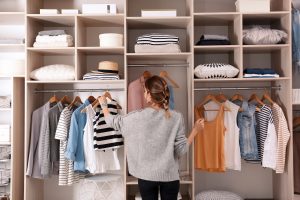 A woman standing in a walk-in closet, looking at her clothing.