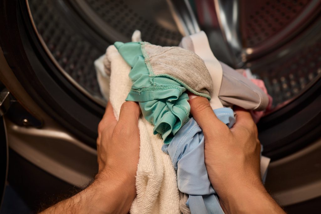 Hands putting clothes into a washing machine.