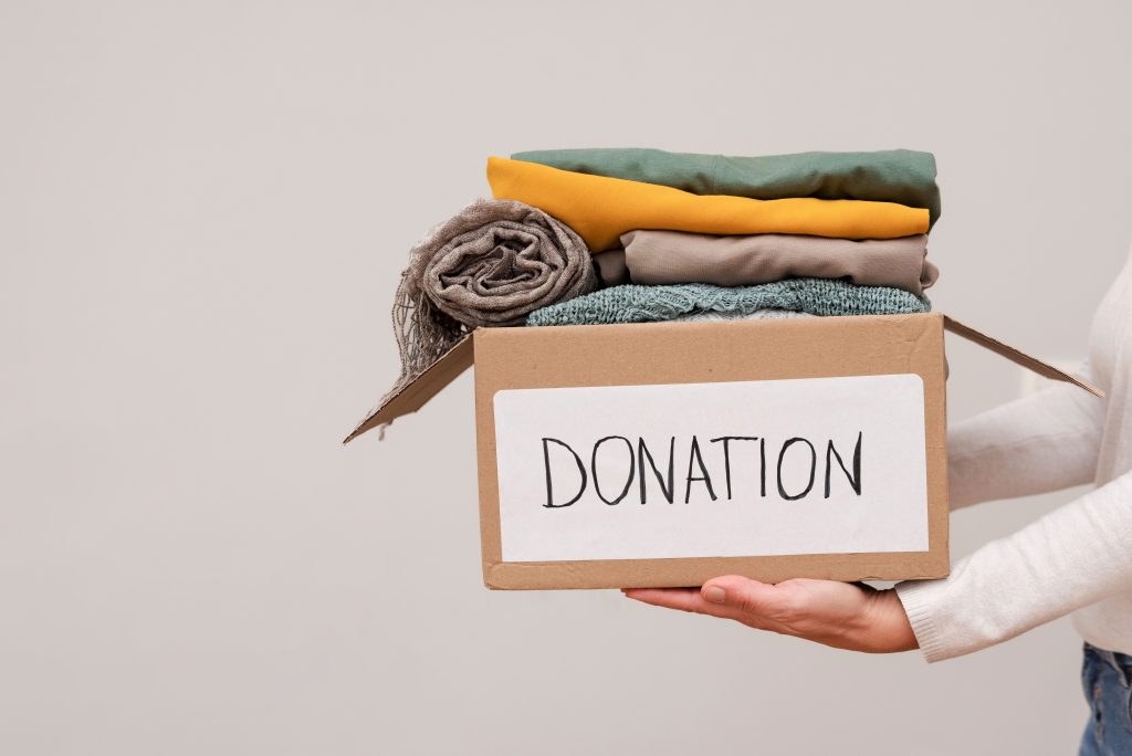 A pair of hands carrying a box marked "donation" and filled with fabric.