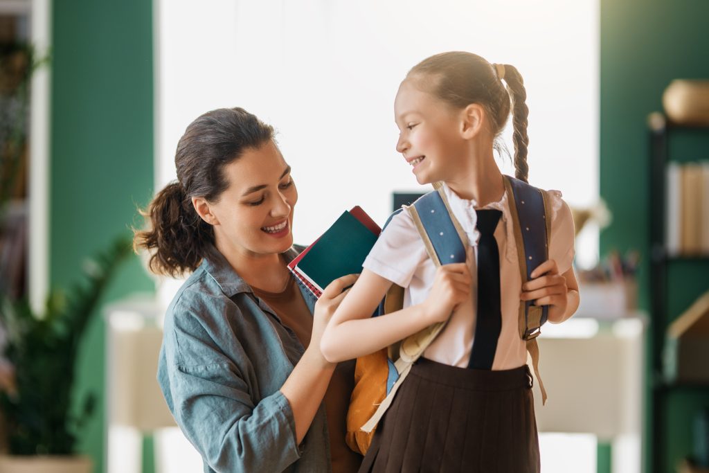 A mom and daughter getting ready for school by putting books in the daughter's backpack.