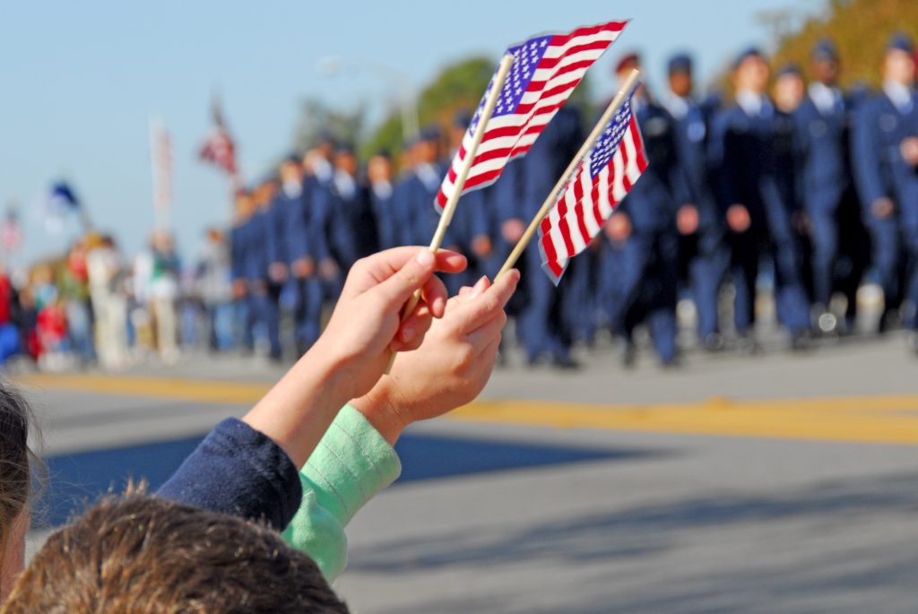 Kids holding up miniature American flags at a Veterans Day parade.