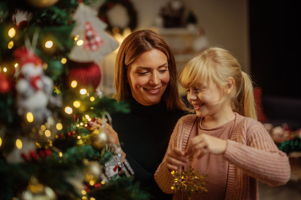 Woman and her young daughter putting ornaments on a Christmas tree.