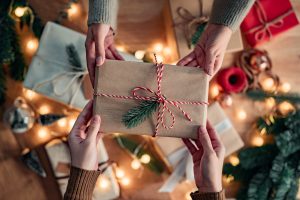 Hands passing a Christmas present to another person.