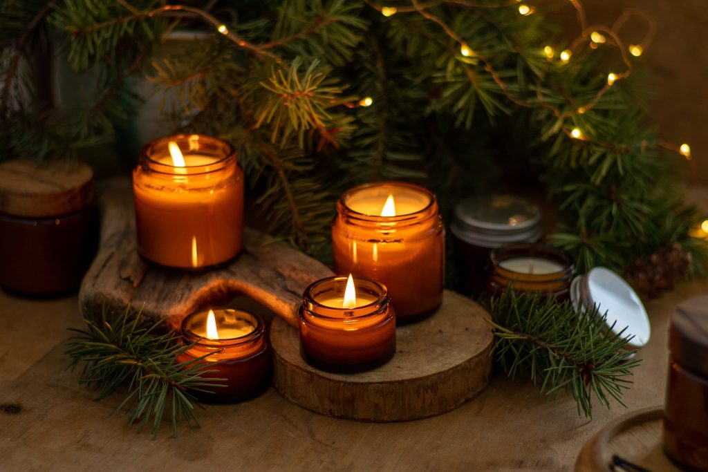 Four small candles burning near the bottom of a christmas tree.