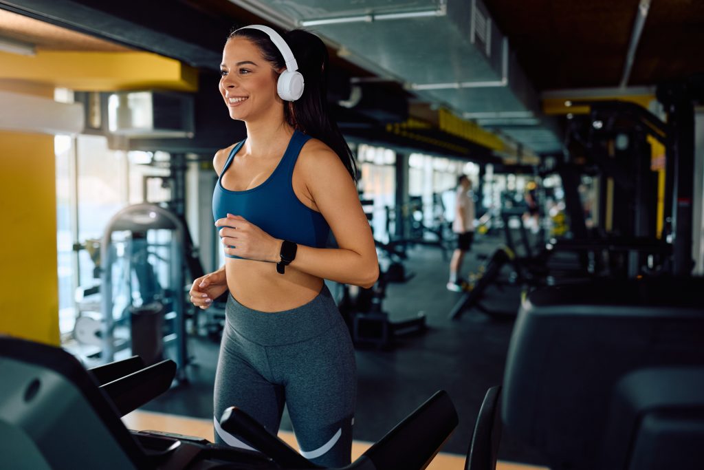 A woman running on a treadmill in a gym while wearing headphones.