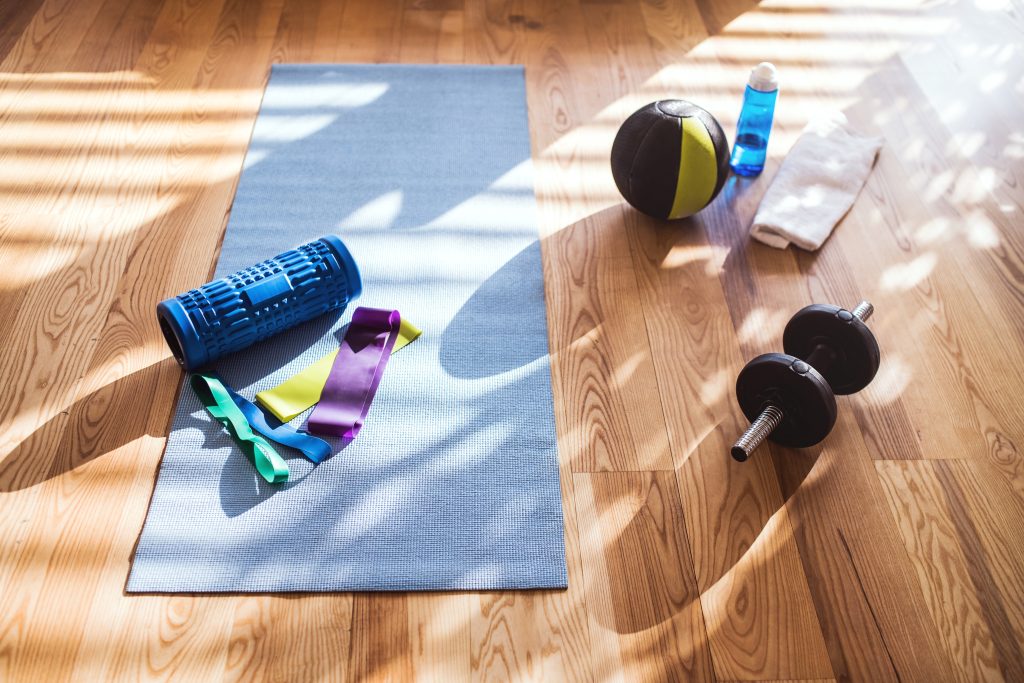 Home gym equipment like a yoga mat, foam roller, dumbbell, and medicine ball.