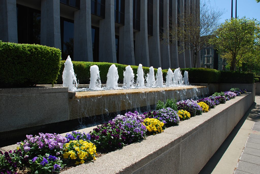 The front facade of a large building with a fountain and blooming flowers.
