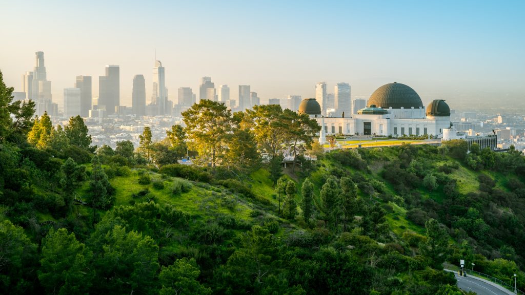 A green hill with Griffith observatory in the foreground, with LA in the background.