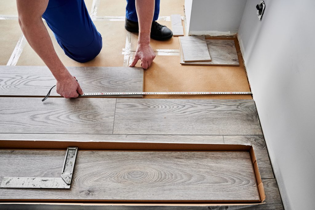 A man kneeling on the floor while measuring floorboards for installation.