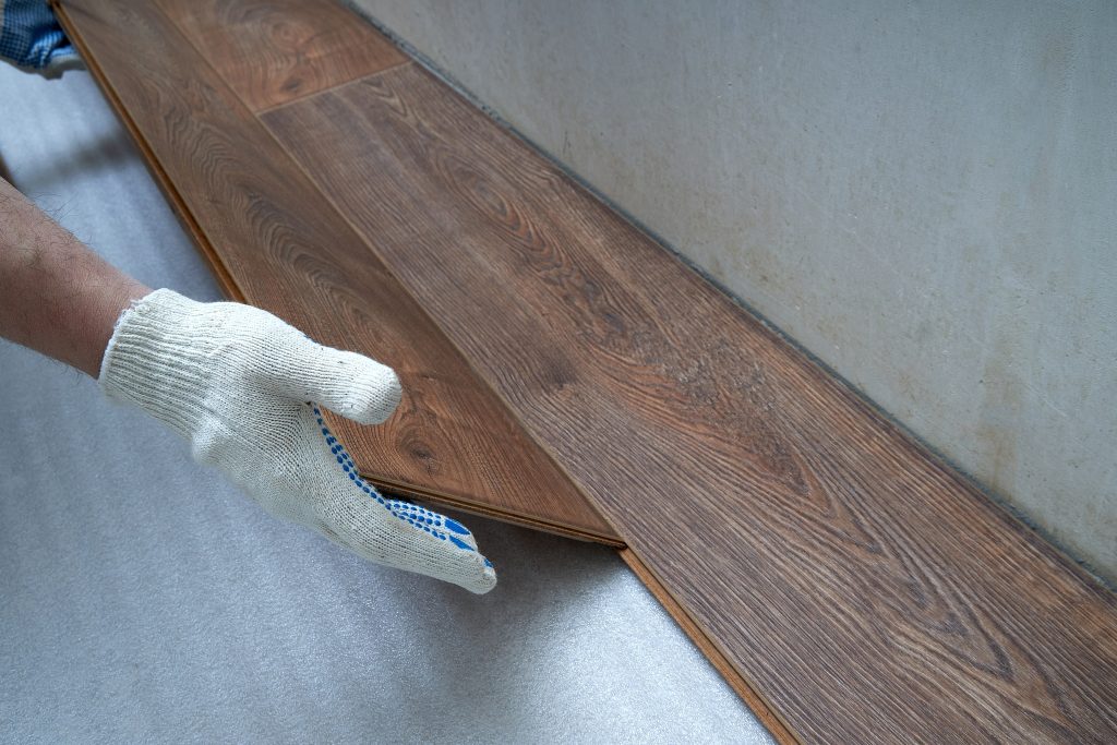 Gloved hands laying down hardwood floorboards.