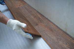 Gloved hands laying down hardwood floorboards.