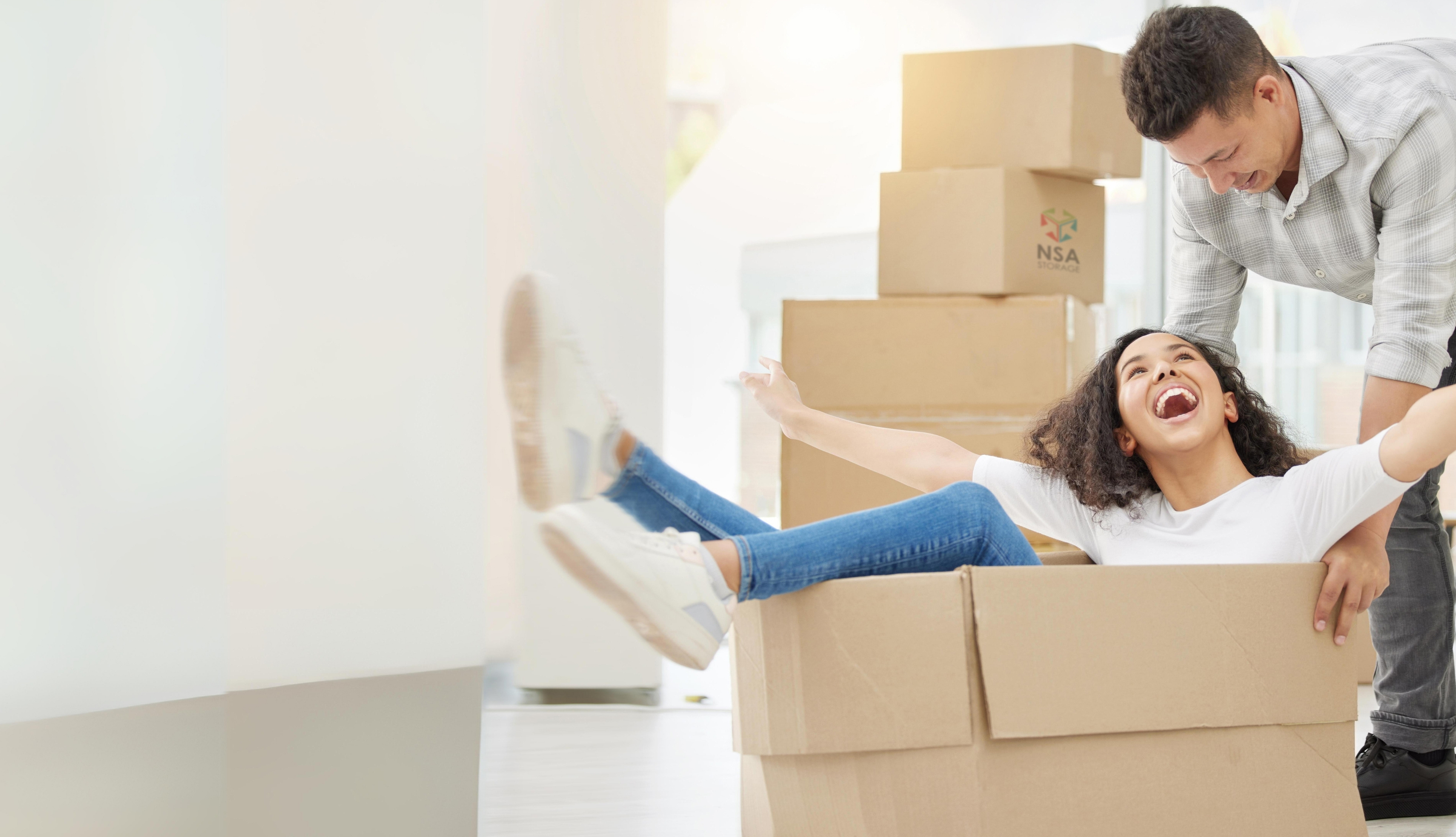 A smiling couple moving cardboard boxes into a new home.
